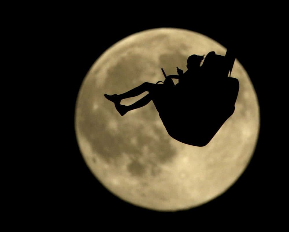 A girl is silhouetted against a rising full moon as she rides an attraction at Worlds of Fun amusement park Thursday in Kansas City, Mo. When the full moon appears at 6:43 a.m. EDT in the U.S. Friday, it will become the second full moon of July, or what's known as a blue moon. (Charlie Riedel/AP)