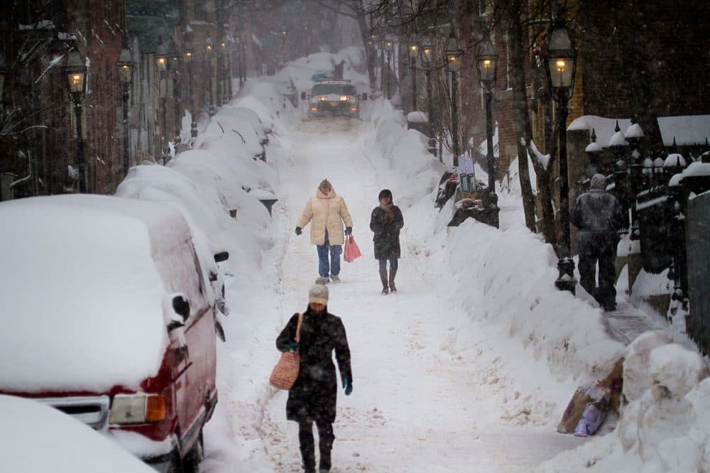 As the days get shorter, New Englanders are haunted by memories of a brutal winter past. In this Feb. 2015 photo, a plow rolls down the street as people trudge forward on foot down Joy Street on Beacon Hill in Boston. (Jesse Costa/WBUR)