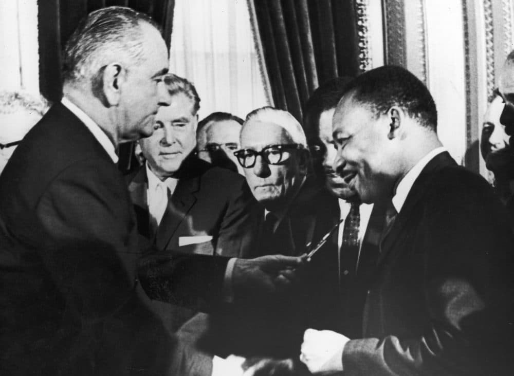 U.S. President Lyndon B. Johnson hands a pen to civil rights leader Rev. Martin Luther King Jr. during the the signing of the voting rights act as officials look on behind them, Washington, D.C., August 6, 1965. (Washington Bureau/Getty Images)