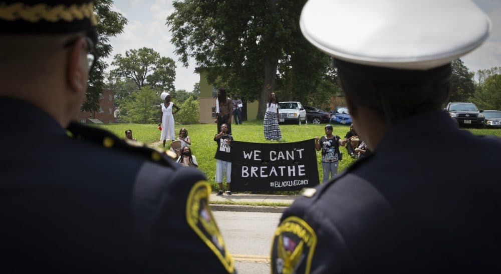 It's time for hard-headed examination of how too many officers treat African-Americans. One place to look for answers, ironically, is Cincinnati. In this photo, Cincinnati police look at protesters across the street from funeral services for Samuel Dubose, Tuesday, July 28, 2015. Dubose was fatally shot by a University of Cincinnati police officer who stopped him for a missing license plate. (John Minchillo/AP)