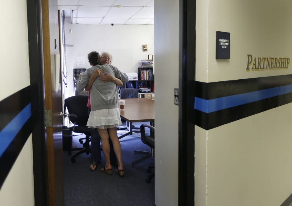 In this July 10, 2015, photo, volunteer Ruth Cote, facing, hugs a woman inside the police station in Gloucester, Mass., who has voluntarily come to the police for help kicking her heroin addiction. Gloucester is taking a novel approach to the war on drugs, making the police station a first stop for addicts on the road to recovery. Addicts can turn in their drugs to police, no questions asked, and officers, volunteers and trained clinicians help connect them with detox and treatment services. (Elise Amendola/AP)