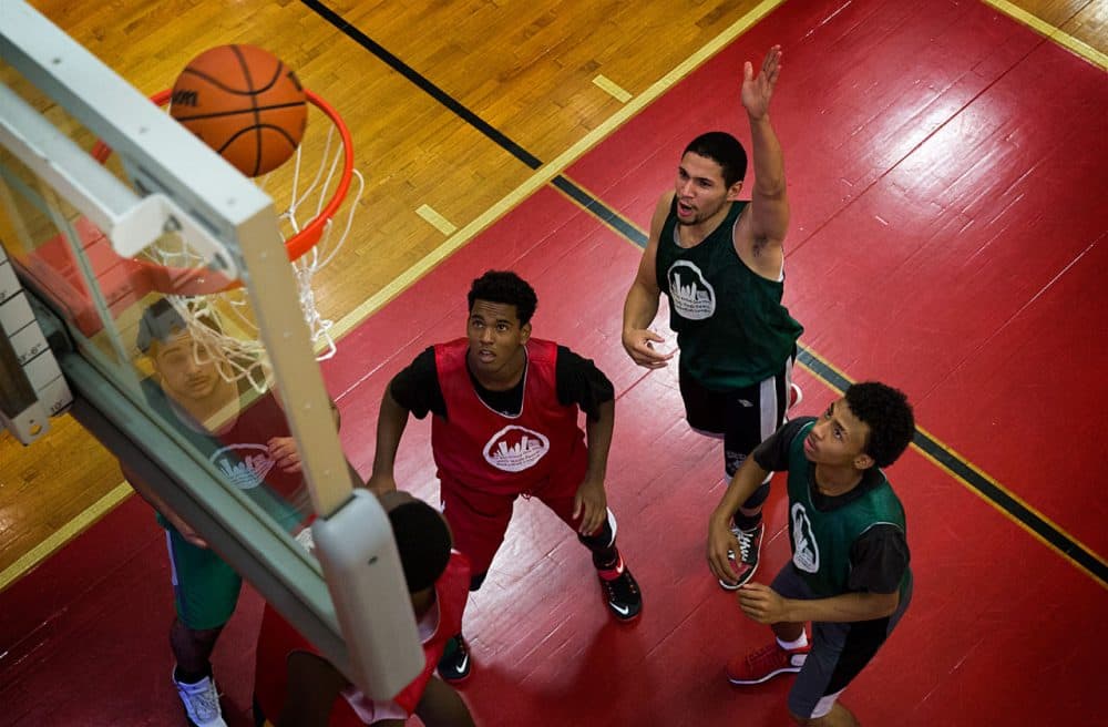 Yasmany Mejia (left), Isaias Ortiz (center) and Jose Cirino (right) watch as the ball drops into the net at the One Hood Peace Basketball League championship. (Robin Lubbock/WBUR)
