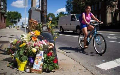 A bicyclist rides past the Boston intersection of Mass. Ave. and Beacon Street, where Anita Kurmann, 38, was hit and killed in a crash on August 7, 2015. Mourners have placed flowers at the scene. (Hadley Green for WBUR)