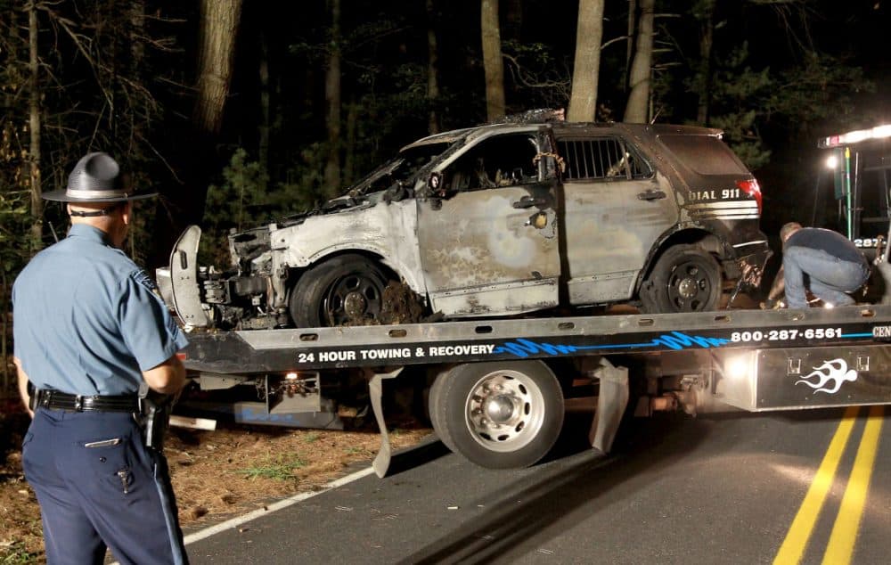 A cruiser that was shot at and burned is removed from Forest Road in Millis on Wednesday evening. Police said Thursday that an unnamed officer shot at his own cruiser and fabricated a suspect description. (John Blanding/The Boston Globe via AP, Pool)