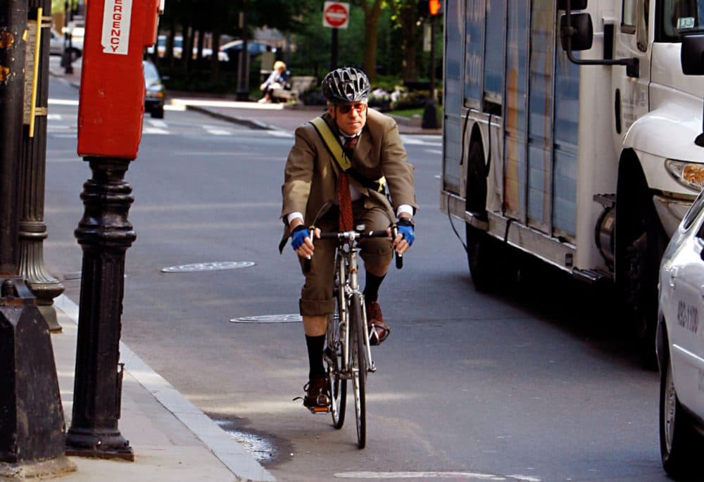 A man rides a bicycle on his morning work commute through downtown Boston, sharing the road with trucks and cars. (AP Photo/Bizuayehu Tesfaye)