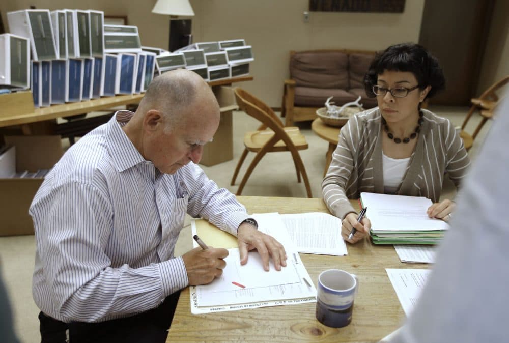California Gov. Jerry Brown signs one of the hundreds of bills he has left to deal with as Graciela Castillo-Krings, right, his deputy legislative secretary, looks on at his Capitol office in Sacramento, Calif., Friday Oct. 9, 2015. (Rich Pedroncelli/AP)