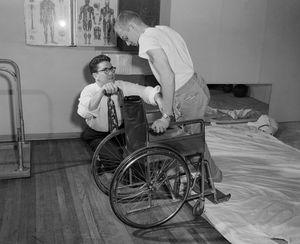 Tim Nugent, head of the paraplegics program at the University of Illinois instructs Glen Perkins, 24, of Morocco, Ind., in how to get in a chair by using only his arms, March 7, 1952. Perkins served two years in The U.S. Navy. He was severely injured in an automobile accident after being discharged from service. (AP Photo/Edward Kitch)
