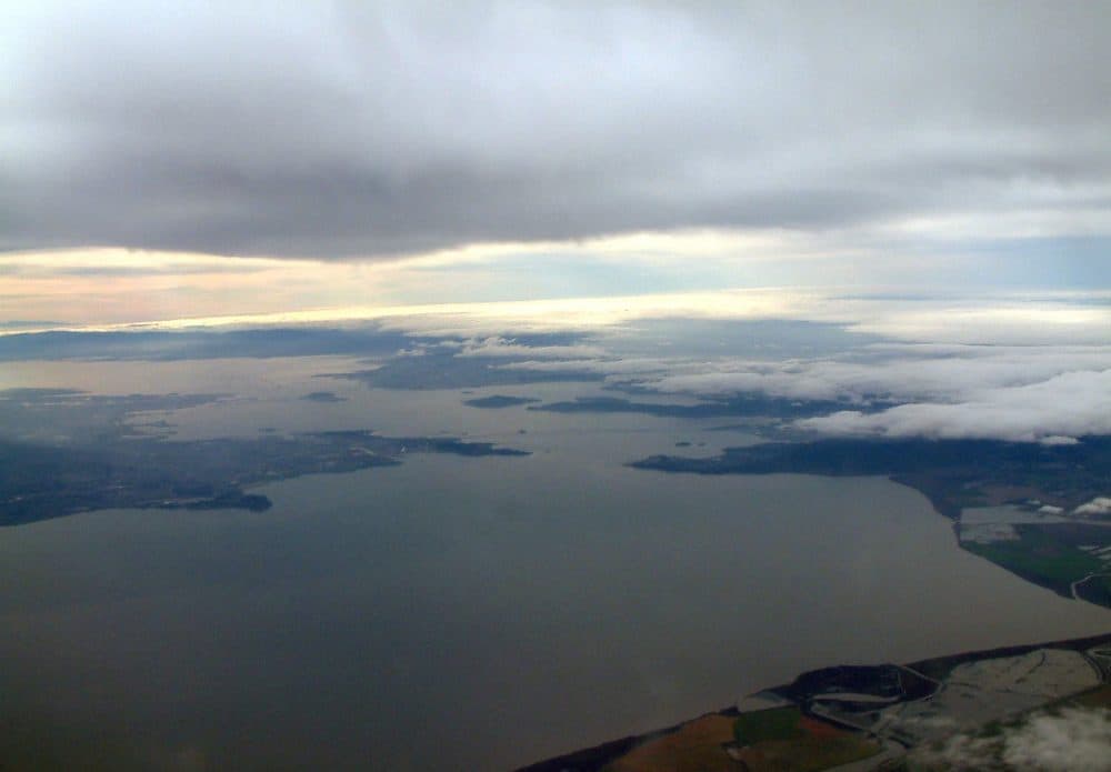 A view out the window of the NOAA research plane, with the Richmond-San Rafael Bridge in the distance. The plane is gaining altitude to fly into the storm cloud. (Danielle Venton/KQED)
