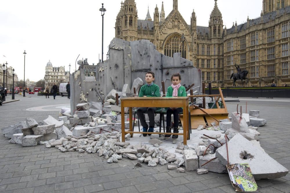 Two children whose school was bombed in Aleppo pose in a mock-up meant to symbolize a destroyed classroom, set up by charity Save the Children outside the Houses of Parliament in London on February 3, 2016 on the eve of a donor conference aiming to raise money for the millions of Syrians hit by the country's civil war and a refugee crisis. (Justin Tallis/AFP/Getty Images)