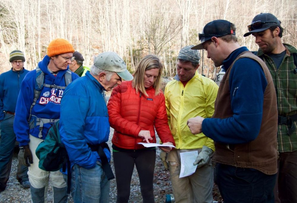 Green Mountain National Forest's Holly Knox, center, and trail designer Hardy Avery, second from right, go over maps that show new backcountry ski trails. Dozens of volunteers have spent the last several weeks clearing trees and brush along the trails. (Nina Keck/VPR)