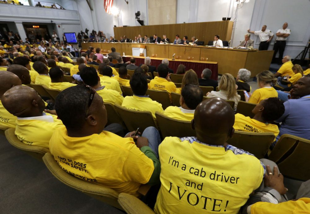 Taxi drivers wearing yellow tee shirts with written messages sit together during a hearing on the regulation of ride handling companies such as Uber and Lyft,  Sept. 15, 2015, at the Statehouse. (Steven Senne/AP)
