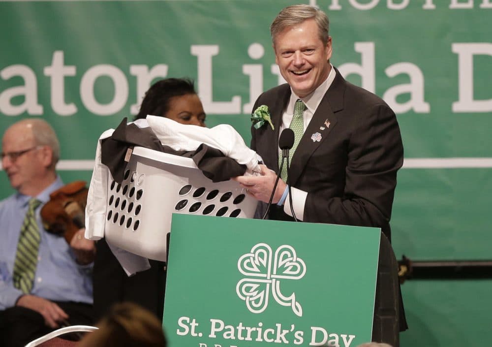 Mass. Gov. Charlie Baker carries a basket of laundry to the podium while making a joke referencing Mass. state Sen. Brian Joyce, D-Milton. Joyce has come under scrutiny for an arrangement with a shop that provided him with free dry cleaning. (Steven Senne/AP)