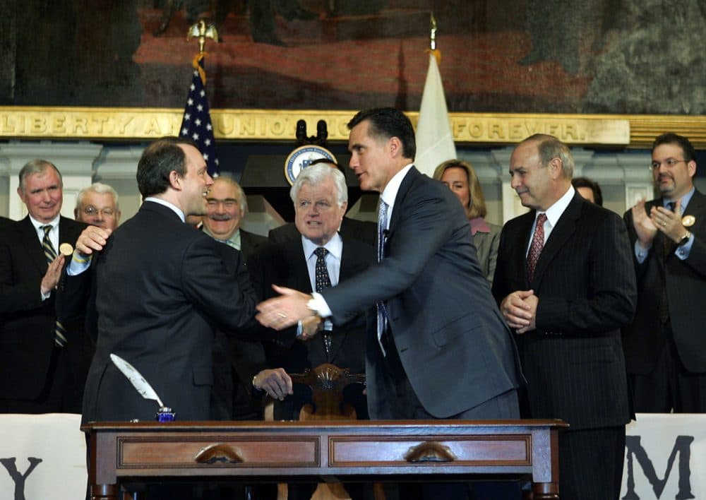 Then-Gov. Mitt Romney shakes hands with other political leaders at Faneuil Hall in Boston after signing into law the state's landmark health reform bill on April 12, 2006. (Elise Amendola/AP)