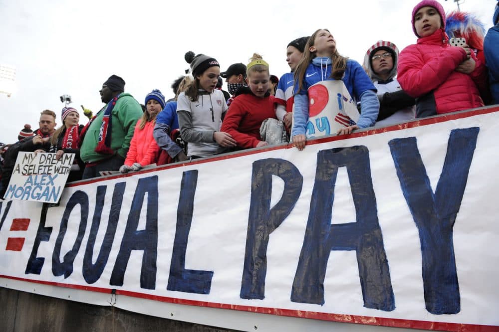 Fans stand behind a large sign for equal pay for the women's soccer team on April 6, 2016, in East Hartford, Conn. (AP Photo/Jessica Hill)