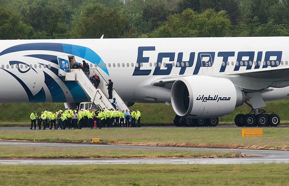 Police escort passengers off the Egyptair Boeing 777 flight from Cairo that was forced to land at Glasgow Prestwick airport in Scotland on June 15, 2013 en route to JFK airport in New York after an onboard incident. Britain's Royal Air Force (RAF) on June 15 escorted an Egyptair plane bound for New York to a Scottish airport following an onboard incident, the Ministry of Defence said. The Boeing 777 was travelling between Cairo and New York when a passenger alerted plane crew that she had found a note reading &quot;I'll set this plane on fire&quot; in the toilet. The message was scrawled in pencil on a napkin and was found by BBC New York producer Nada Tawfik. (Andy Buchanan/AFP/Getty Images)