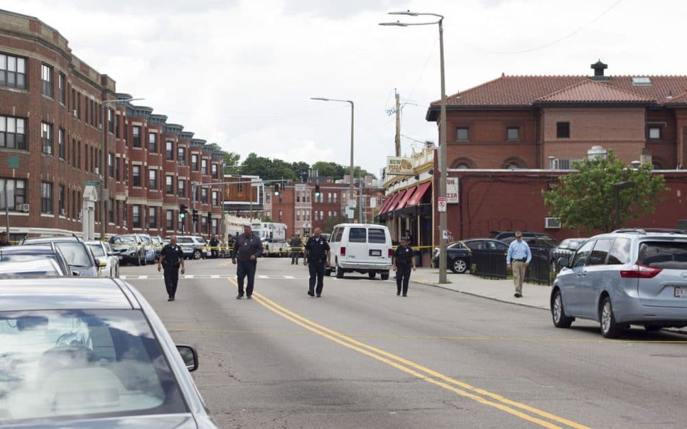 Police scan the scene where a Boston high school student was killed and three others wounded in a shooting on Washington Street in Dorchester. (Joe Difazio for WBUR)