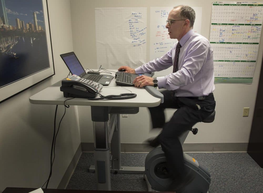 Dr. Eddie Phillips rides an exercise bike as he works in his office at the VA Boston Healthcare System. (Robin Lubbock/WBUR)