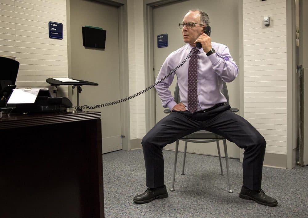 Dr. Eddie Phillips squats as he talks on the phone at his office. (Robin Lubbock/WBUR)