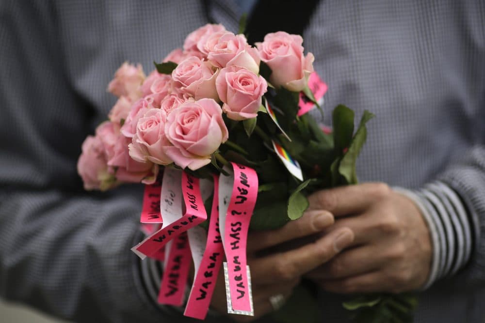 A man holds a bunch of flowers with small ribbons reading 'Why Hatred? If there is love.' during a vigil in front of the United States embassy in Berlin, German, on Monday to honor the victims. (Markus Schreiber/AP)
