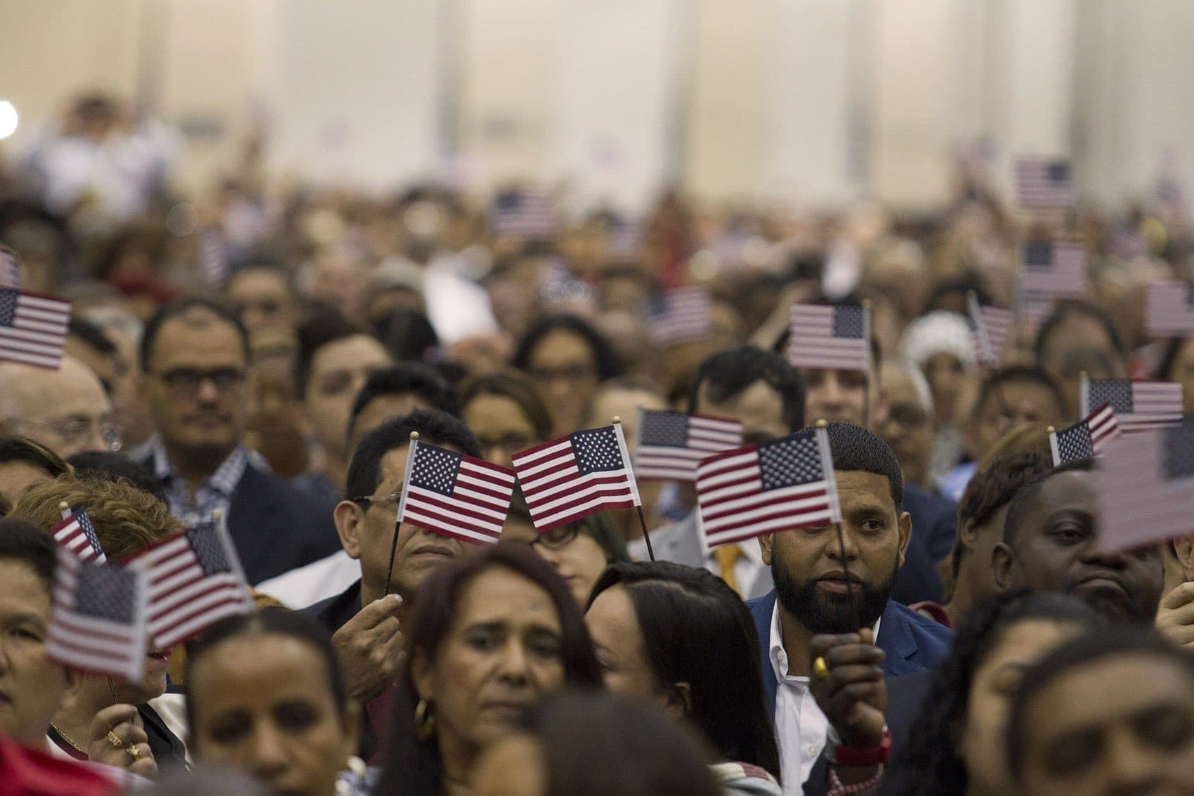 New U.S. citizens wave flags during a rendition of “America the Beautiful” at the Hynes Convention Center Thursday. (Joe Difazio for WBUR)