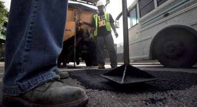 A proposed tax on incomes over $1 million will fund Massachusetts schools and infrastructure. Unless, of course, it won't. 
 Pictured: Boston Public Works workers Victor Duret, feet only at left, and Tyrone Odom, behind, both of Boston, fill a pothole with asphalt in Boston's Charlestown neighborhood. (Steven Senne/AP)