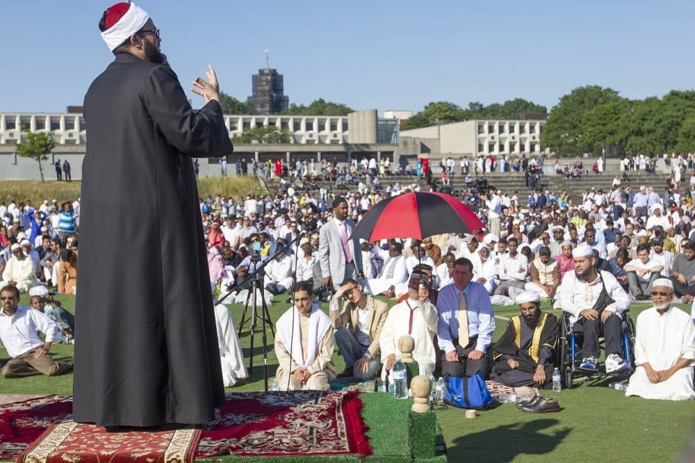 Imam Yasir Fahmy speaks at an Eid prayer service at Madison Field, across from the Islamic Society of Boston Cultural Center, on Wednesday morning. Mayor Marty Walsh (underneath the umbrella) listens. (Joe Difazio for WBUR)