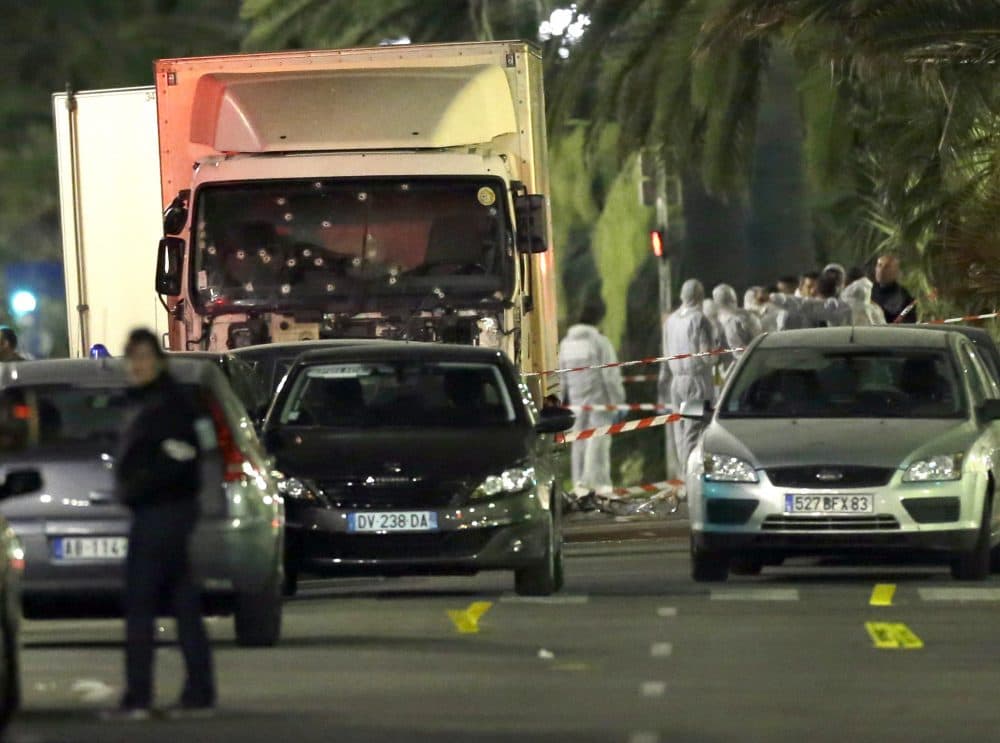 Forensic officers stand near a truck with its windscreen riddled with bullets, that plowed through a crowd of revelers who'd gathered to watch the fireworks in the French resort city of Nice, southern France, Friday, July 15, 2016. At least 80 people were killed before police killed the driver, authorities said. (Claude Paris/AP)
