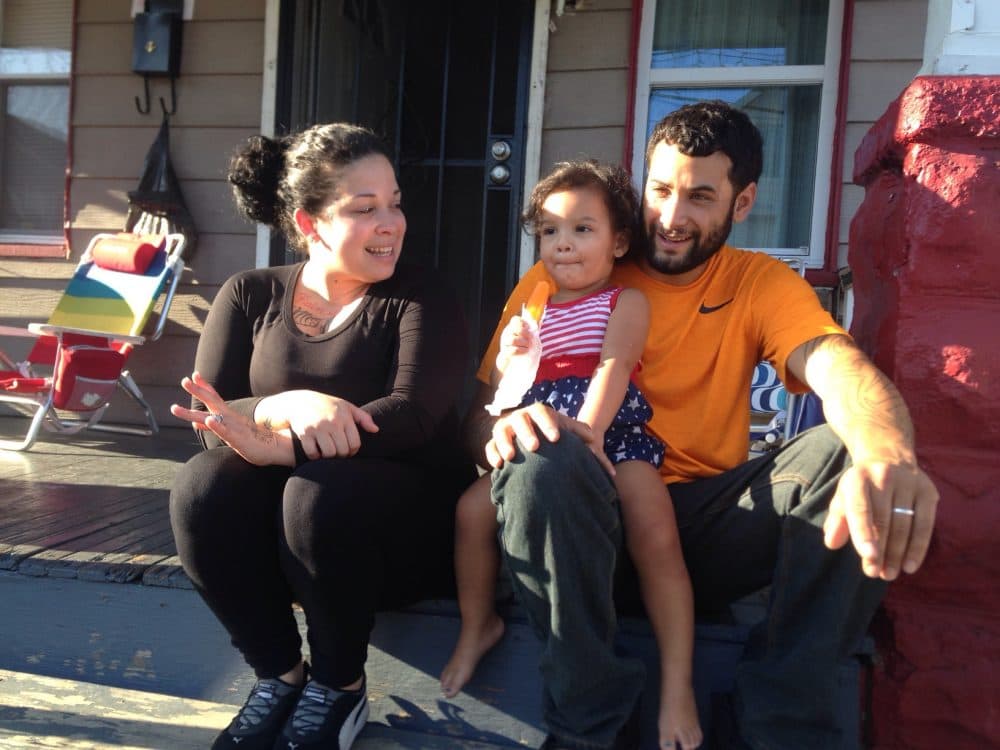 Cinthia Cruz (left) and her boyfriend Juan Rivera sit on their front steps with their daughter Zahira. Cruz and Rivera live in Cleveland, and make $1,400 a month to support their family.  (Peter O'Dowd/Here & Now)