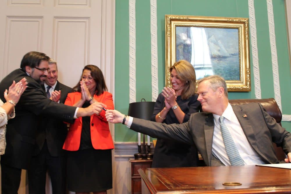 After signing legislation to regulate the state's ride-hailing industry, Gov. Charlie Baker thanked Deputy Chief of Staff Joel Barrera for his role in advancing the measure, and handed him the first pen he used to sign the bill into law. (Antonio Caban/State House News Service)