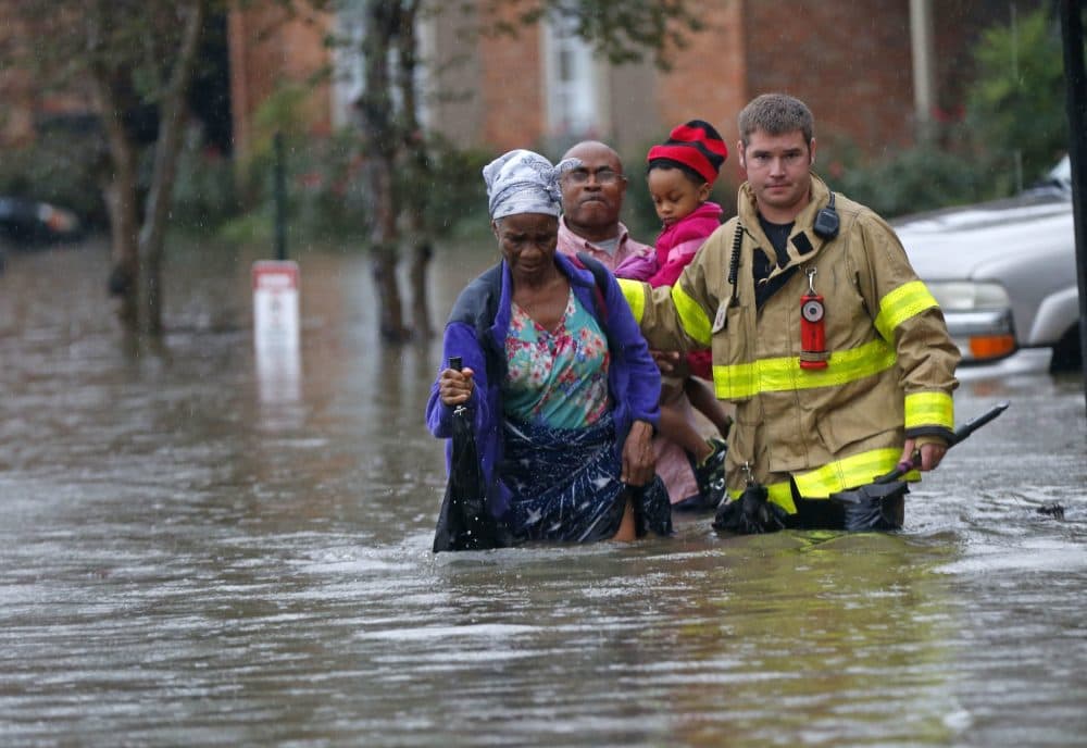 A member of the St. George Fire Department assists residents as they wade through floodwaters from heavy rains in Baton Rouge, Louisiana on Friday, Aug. 12, 2016. (Gerald Herbert/AP)
