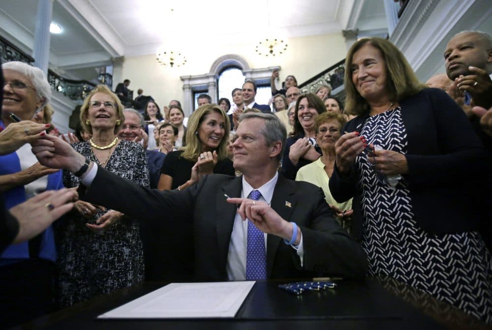 Gov. Charlie Baker hands out pens to supporters, including state Treasurer Deborah Goldberg, right, after signing a bill into law at the State House Monday that requires men and women be paid equally for comparable work in Massachusetts. (Elise Amendola/AP)