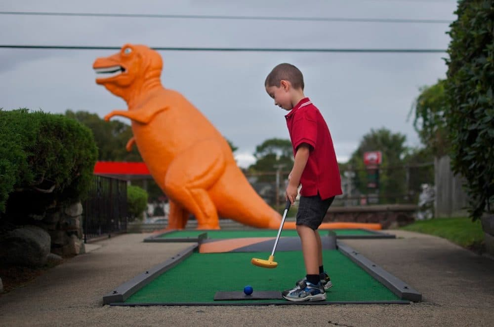 After more than 50 years, the old-fashioned miniature golf course off Route 1 in Saugus is closing. The spot is well known for its DayGlo orange T-rex that, from the sixth hole, gazes over the highway. Here, Louie Schraffa, 5, of East Boston, prepares for a putt on the dinosaur hole, Sept. 29, 2015. (Sharon Brody/WBUR)