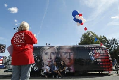 People pose for a photo kneeling near a bus adorned with photos of candidates Hillary Clinton and Donald Trump before the presidential debate at Hofstra University in Hempstead, N.Y., Monday, Sept. 26, 2016. (Mary Altaffer/AP)