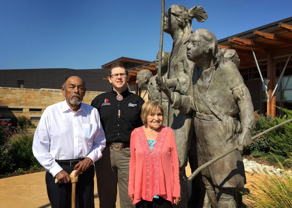 Chickasaw tribal elders Jerry Imotichey (left) and Hannah Pitmon (right) stand with Joshua Hinson (middle), director of the Department of Chickasaw Language, in front of &quot;The Arrival&quot; statue at the Chickasaw Cultural Center in Sulphur, Okla. (Karyn Miller-Medzon/Here & Now)