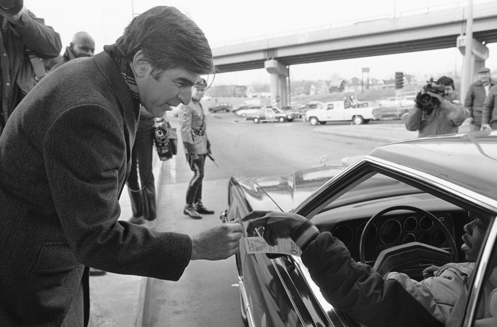 Former Massachusetts Gov. Michael Dukakis speaks to a motorist at a Massachusetts Turnpike toll booth in Boston in 1985 as he hands out pamphlets reminding people of the new state law requiring automobile occupants to use seat belts. (John Pawlick/AP)