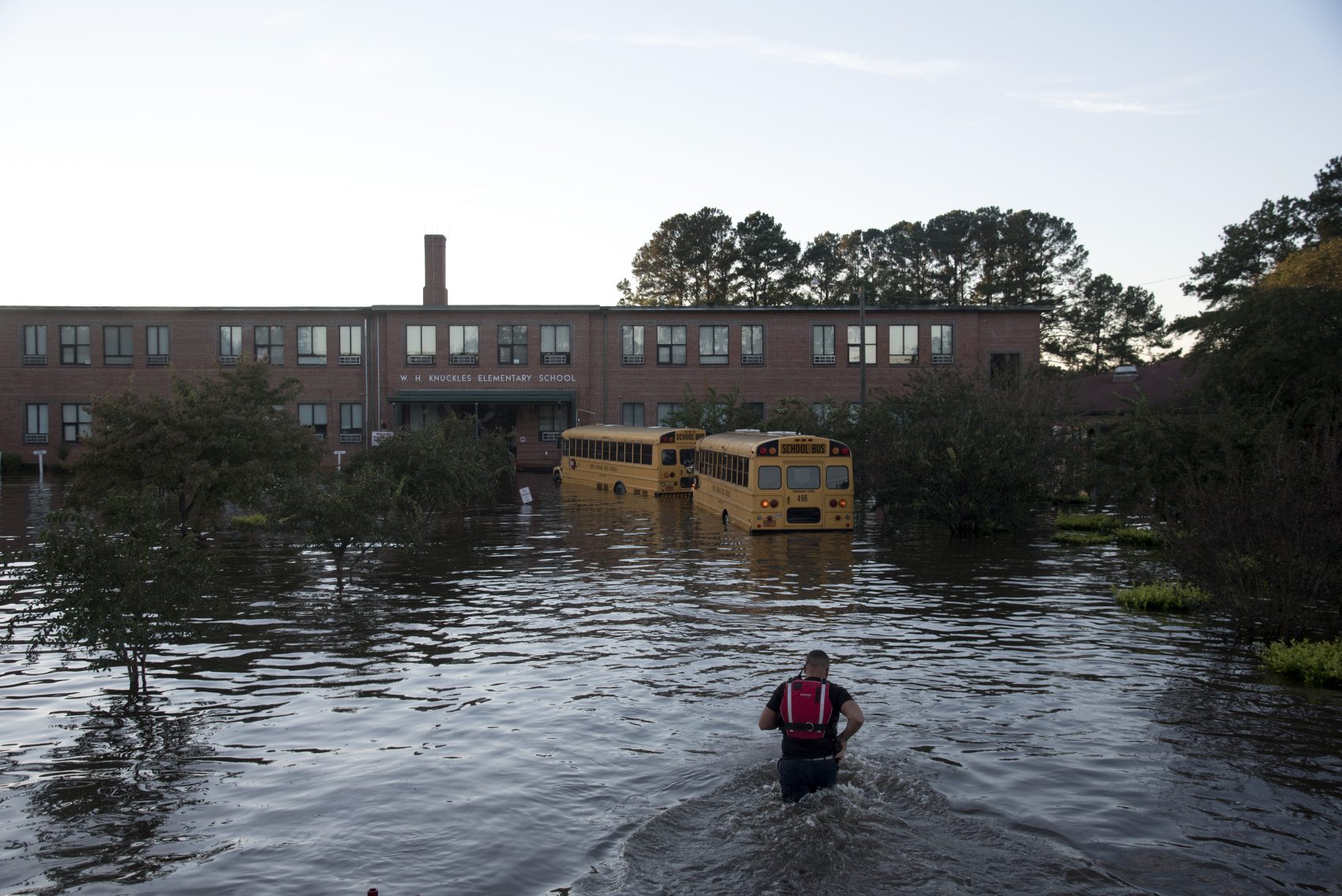 A volunteer firefighter with the Raynham-McDonald Fire Department makes his way through floodwaters caused by rain from Hurricane Matthew to turn off the lights of a school bus in front of W.H. Knuckles Elementary School in Lumberton, N.C., Monday, Oct. 10, 2016. (Mike Spencer/AP)