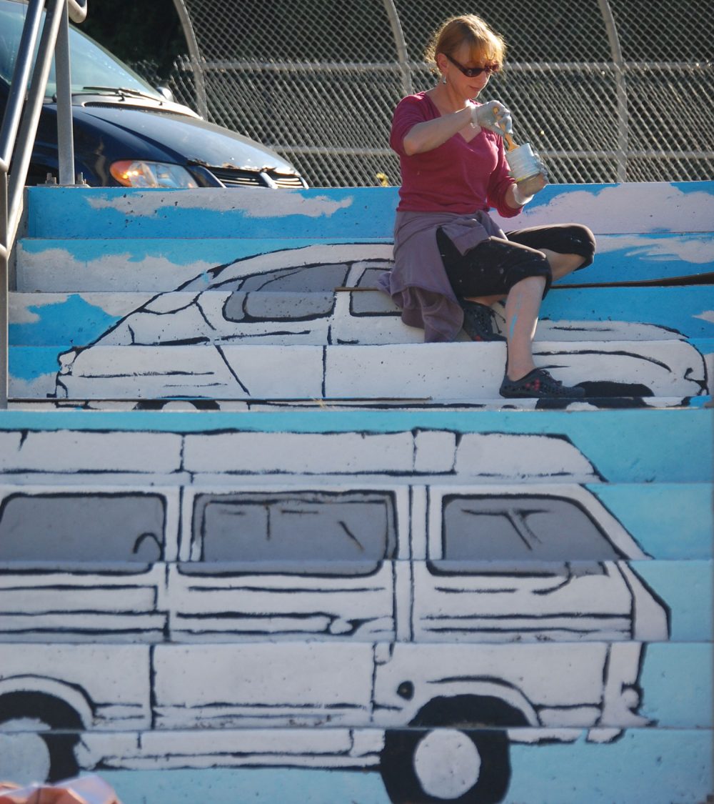 Liz LaManche paints “The Soul’s Journey as a Series of Weird Old Automobiles&quot; in the park at the intersection of Pearl and Medford streets in Somerville. (Greg Cook)