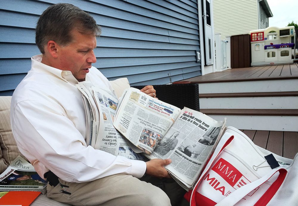 At his home in Haverhill, Colin LePage leafs through newspapers he shows to middle-schoolers to educate them about the dangers of drugs. (Martha Bebinger/WBUR)