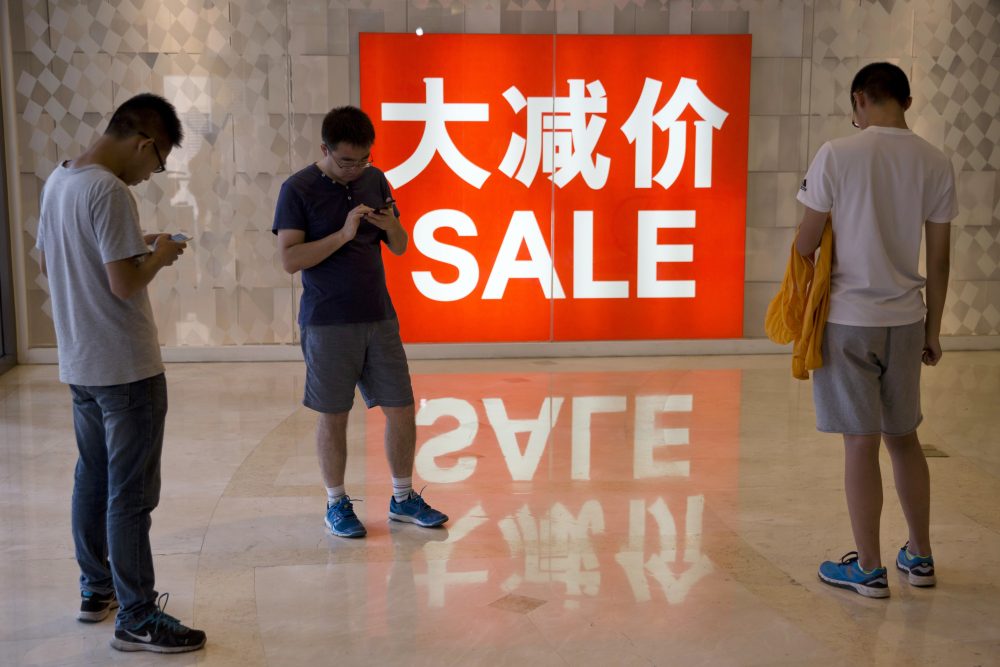 In this July 10, 2016 file photo, Chinese shoppers stand near a sale advertisement at a shopping area in Beijing. The world’s second-largest economy grew by 6.7 percent in the three months ending in September compared with a year earlier, data showed Wednesday, Oct. 19, 2016. (Ng Han Guan/AP)