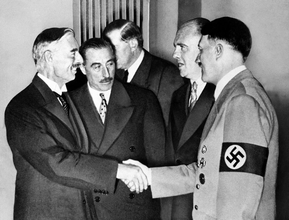 Hands clasped in friendship, Adolf Hitler and England's Prime Minister Neville Chamberlain, are shown in this historic pose at Munich on Sept. 30, 1938.   This was the day when the premier of France and England signed the Munich agreement, sealing the fate of Czechoslovakia.   Next to Chamberlain is Sir Neville Henderson, British Ambassador to Germany.   Paul Schmidt, an interpreter, stands next to Hitler. (AP Photo)