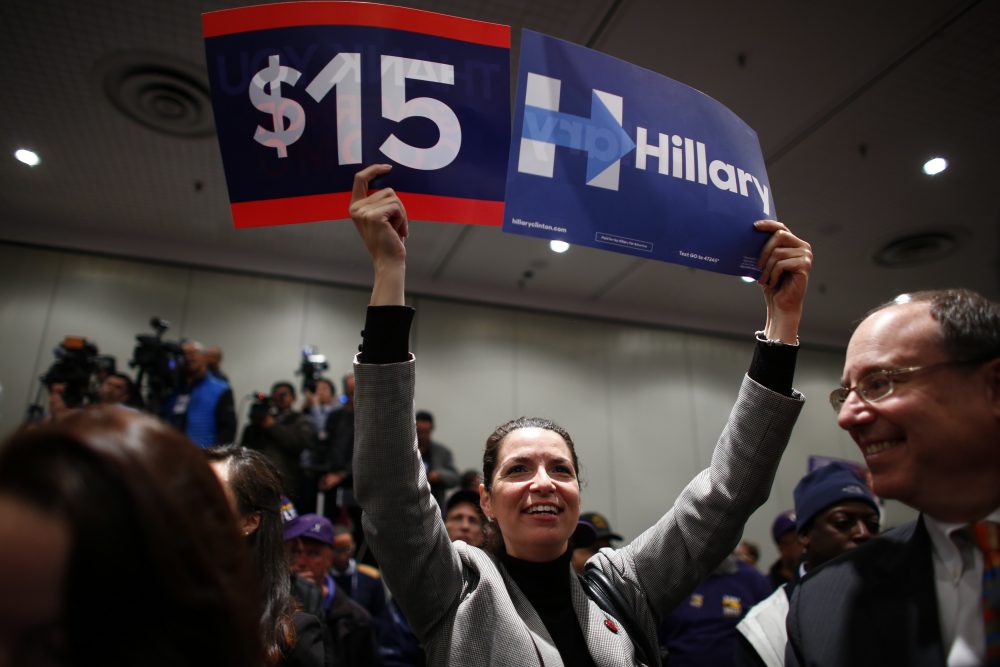 A woman holds banners in support of a $15 minimum wage as Democratic presidential candidate Hillary Clinton speaks during a event at the Javitz Center in New York on April 4, 2016. (Kena Betancur/AFP/Getty Images)