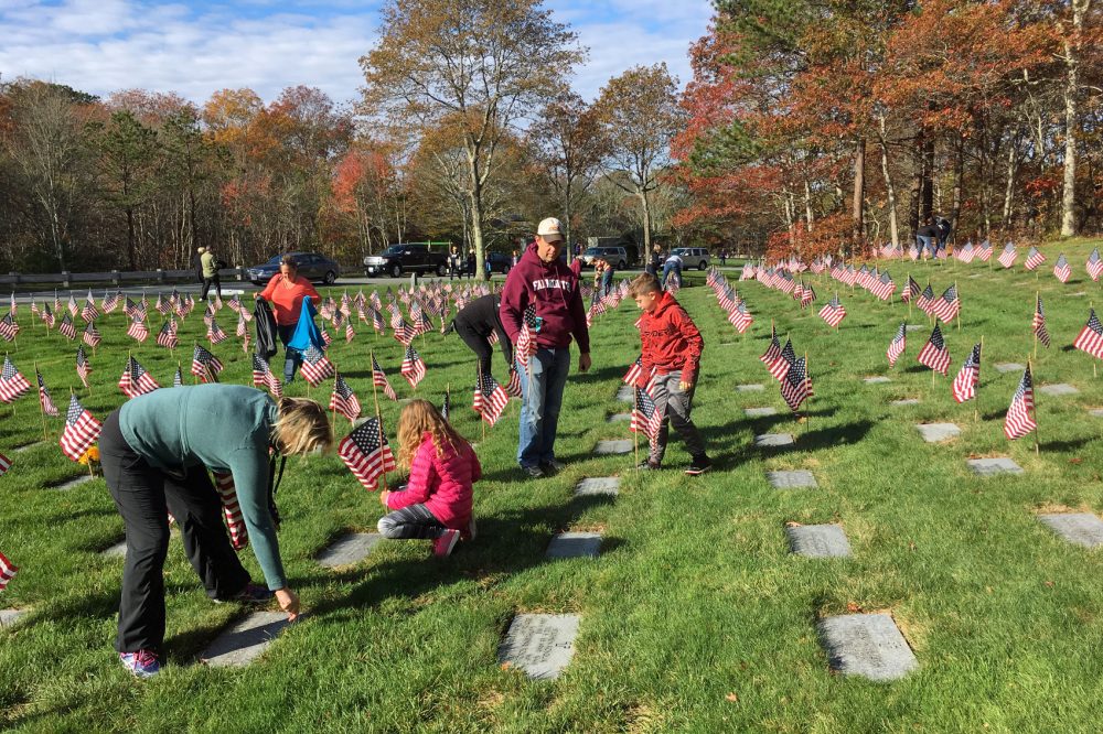 Volunteers place American flags on the graves at the Massachusetts National Cemetery in Bourne, Mass., for Veterans Day. (Alex Ashlock/Here & Now)