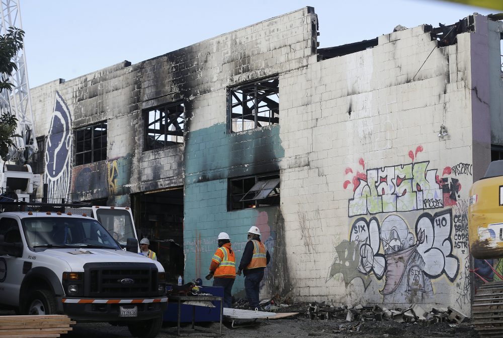 Emergency crew workers walk in front of the site of a warehouse fire in Oakland, Calif., Tuesday, Dec. 6, 2016. The fire erupted Friday, Dec. 2, killing dozens. (Jeff Chiu/AP)