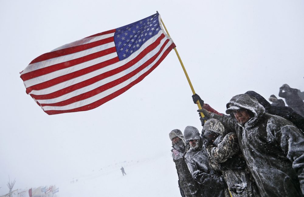 Military veterans huddle together to hold an American flag against strong winds during a march to a closed bridge outside the Oceti Sakowin camp where people have gathered to protest the Dakota Access oil pipeline in Cannon Ball, N.D., Monday, Dec. 5, 2016. (David Goldman/AP)
