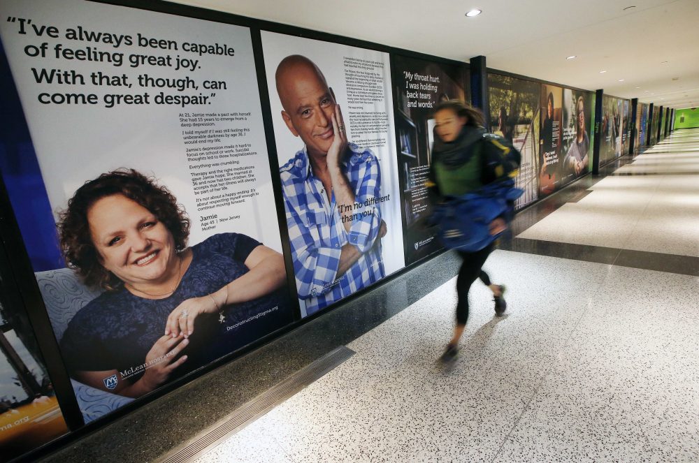 A passenger rushes past a new art exhibit at Logan Airport that consists of larger-than-life posters of nearly three dozen people who have struggled with mental illness. (Michael Dwyer/AP)