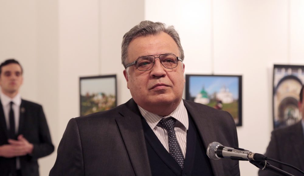 The Russian Ambassador to Turkey Andrei Karlov speaks a gallery in Ankara Monday Dec. 19, 2016. A gunman opened fire on and killed Russia's ambassador to Turkey Karlov at a photo exhibition on Monday. The gunman is seen at rear on the left. (Burhan Ozbilici/AP)
