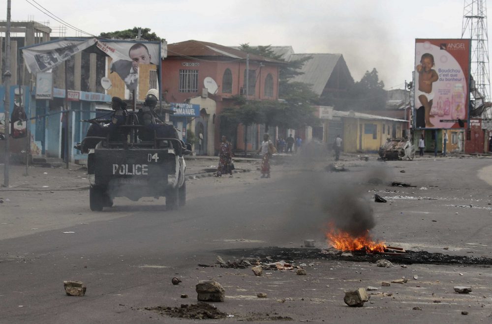 Policemen drive past burning debris during protests in Kinshasa, Democratic Republic of Congo, Tuesday, Dec. 20, 2016. (John Bompengo/AP)