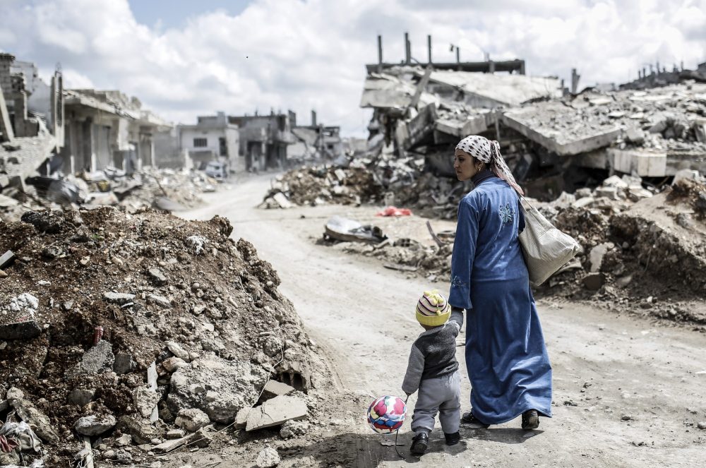 A Kurdish Syrian woman walks with her child past the ruins of the town of Kobane, also known as Ain al-Arab, on March 25, 2015. (Yasin Akgul/AFP/Getty Images)