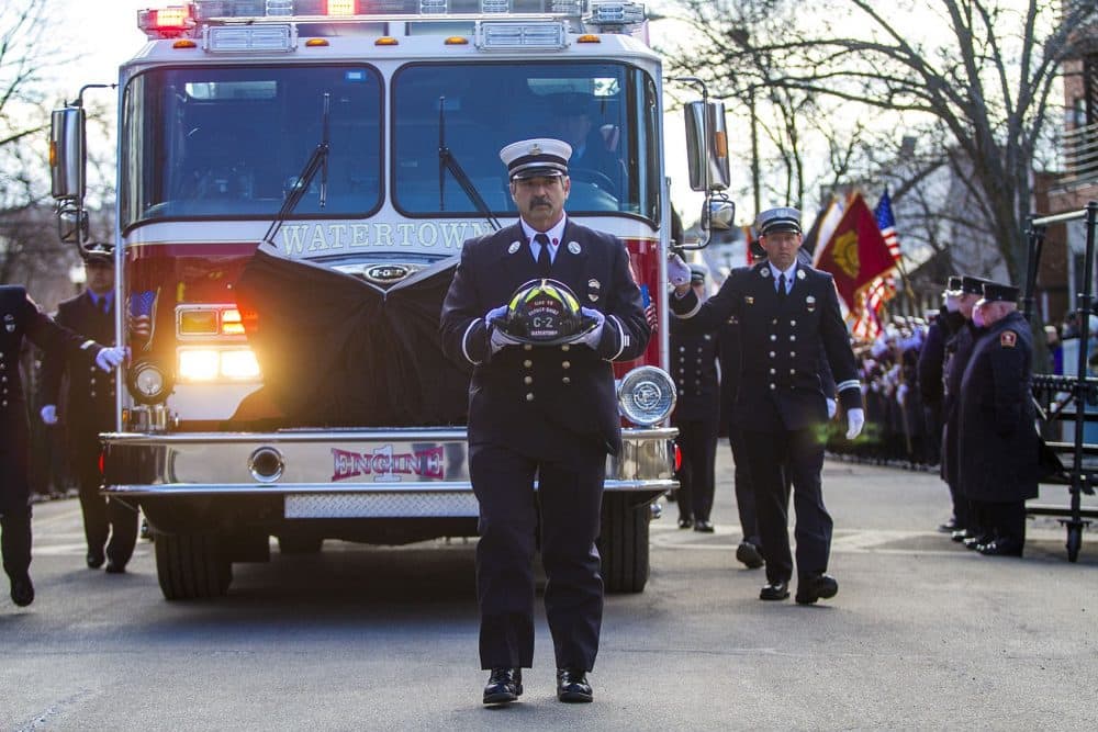Watertown Lt. John Baccari carries the helmet of fallen Watertown firefighter Joseph Toscano as the funeral procession arrives at St. Patrick's Church Wednesday. Toscano collapsed while fighting a house fire on Friday. (Jesse Costa/WBUR)