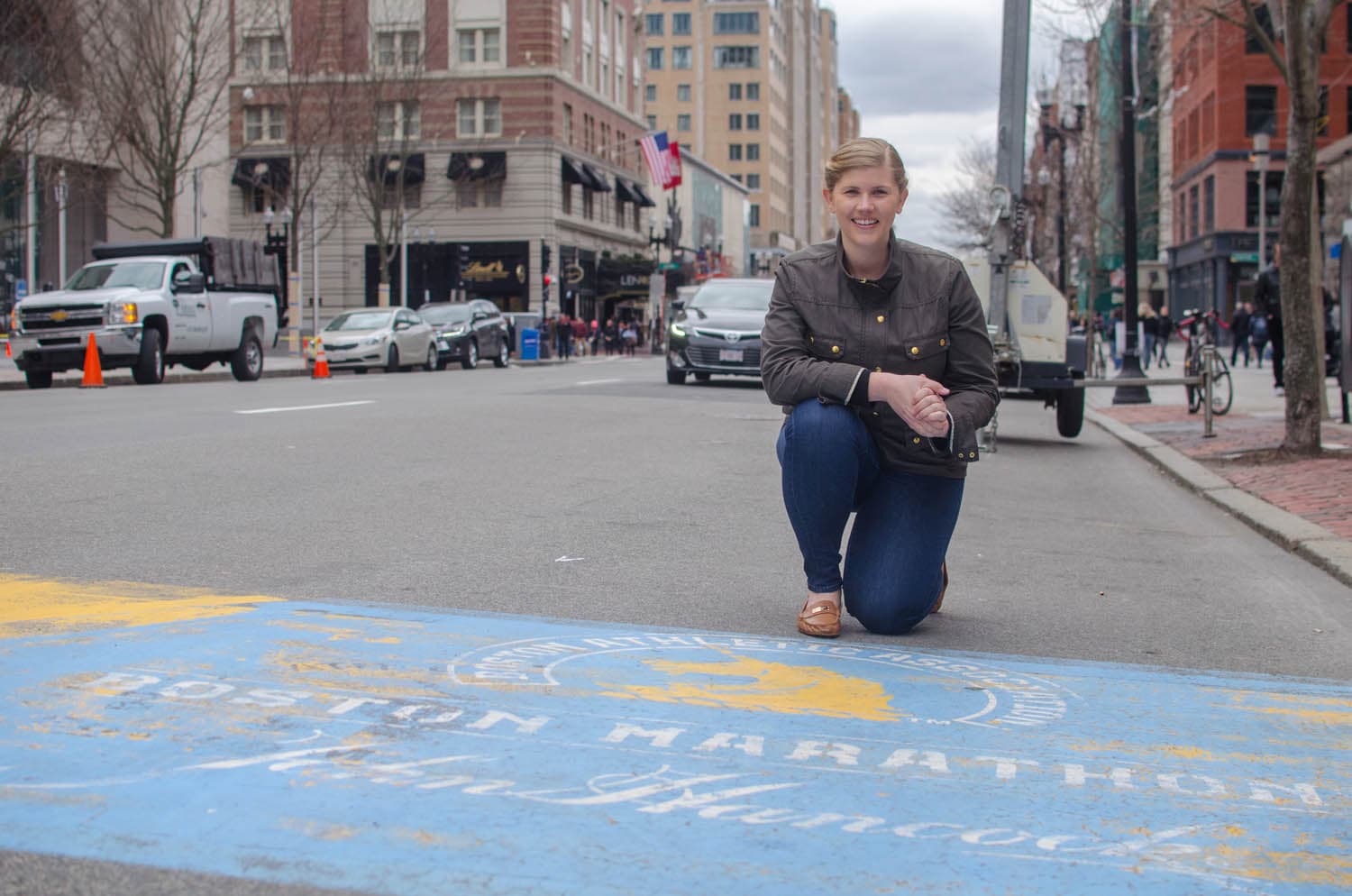 Meghan Connors kneels at the finish line of the Boston Marathon on Boylston Street. This year she's running her fifth Boston Marathon, supporting the MGH Pediatric Oncology division where she was treated for neuroblastoma when she was three years old. (Sharon Brody/WBUR)